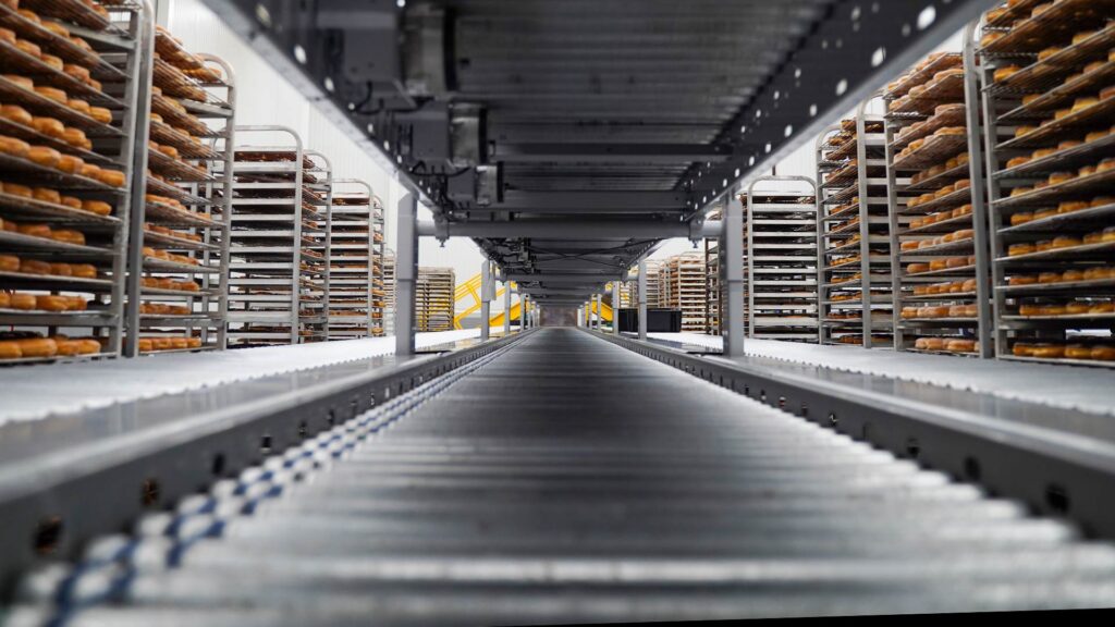 QuikTrip Doughnut Line|Food & Beverage Blue Background|Quik Trip production line|Quik Trip Training Room with workstations and video display|Stainless steel ovens and portable racks filled with baked rolls|Quik Trip production line with blue food grade conveyor belt|Quik Trip conveyor system flanked by portable racks filled with baked goods|Troughed conveyor with food grade blue belt||||||||