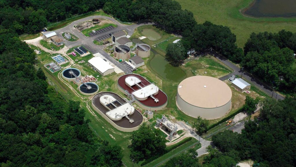 Aerial photo of the Live Oak Wastewater Treatment Plant|Exterior photo of water storage at the Live Oak Wastewater Treatment Plant. Staircase leads up to platform.|In-ground concrete water treatment tanks. Survival ring hanging on railing.|Aerial photo of the Live Oak Wastewater Treatment Plant||||