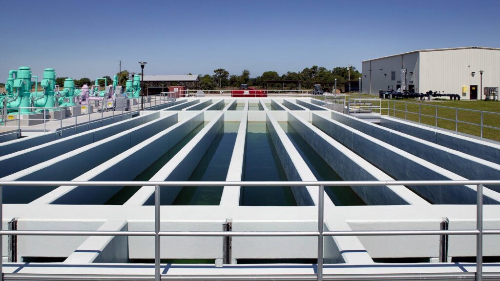 Exterior photo of aeration basins at the Winter Haven Wastewater Treatment Plant|Green motors and pipes next aeration basins.|Interior photo of the facility with large white tanks. Men in hardhats checking their status.|Aerial view of Winter Haven Wastewater Treatment Plant|Exterior photo of aeration basins of water at the Winter Haven Wastewater Treatment Plant|Green pipes and motors outside the facility||||||
